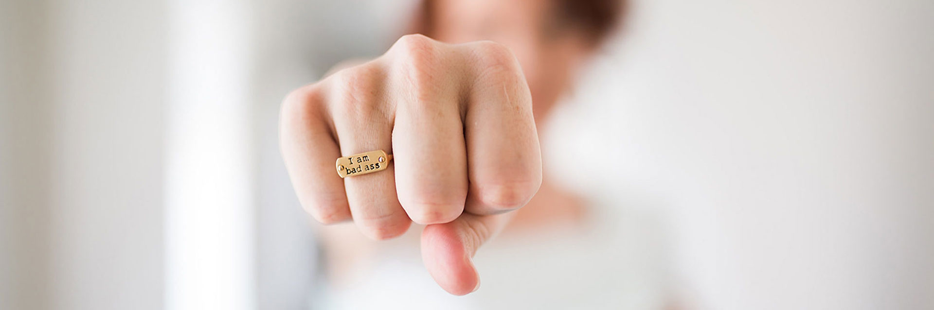 A women's hand held forward in a fist bump with a ring that says I am bad ass.